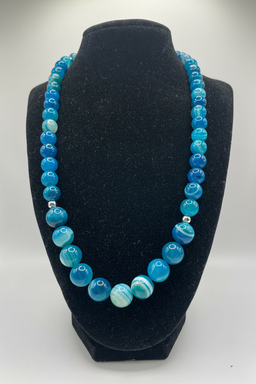 Blue beaded necklace on a black bust against a white background