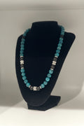 Necklace with blue and black beads on a black stand against a white background