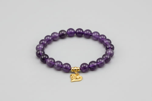 Purple beaded bracelet with a gold heart charm on a gray background