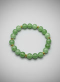 Green beaded bracelet with gold accents on a light gray background