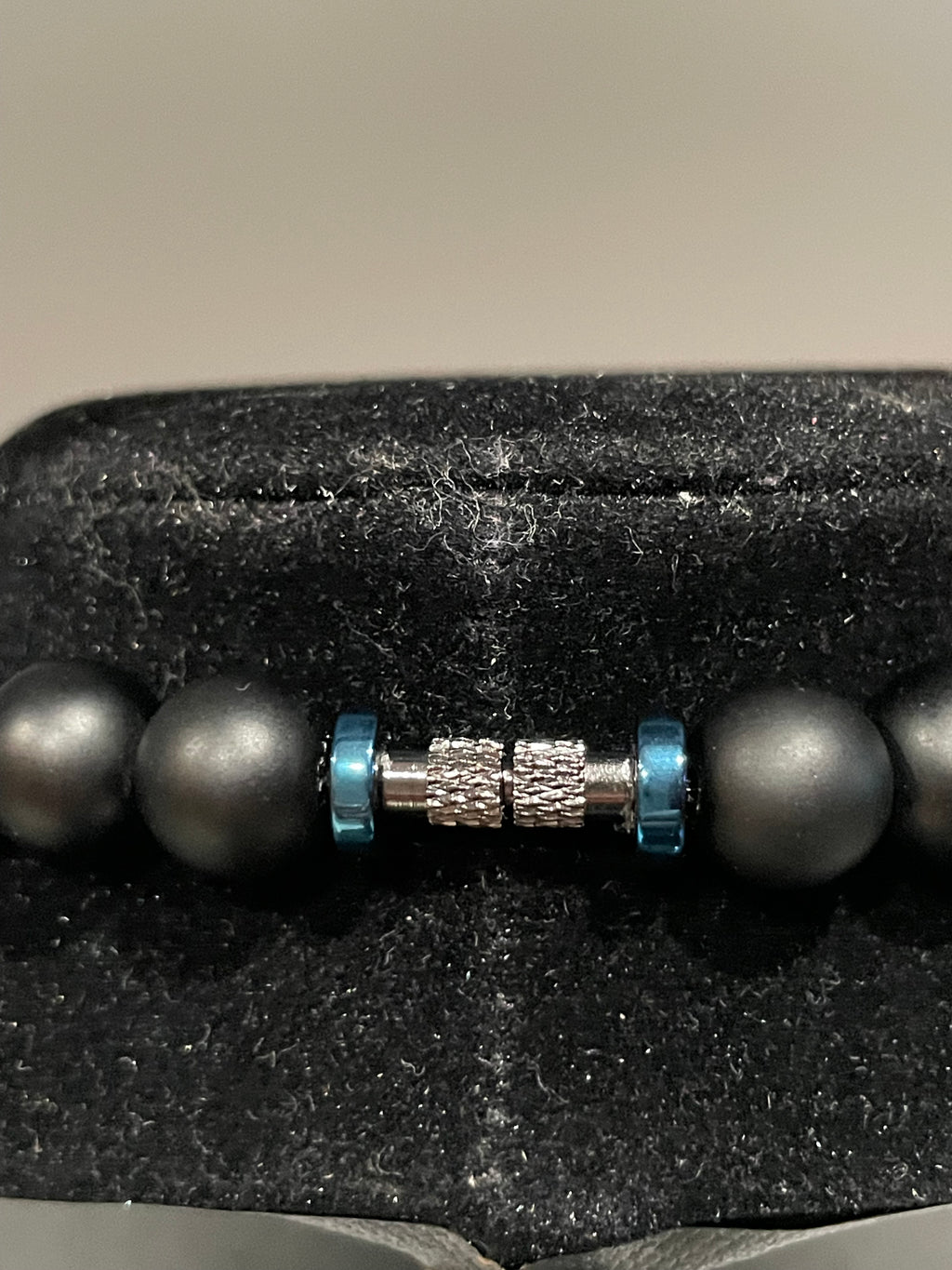 Close-up of a black beaded black metallic screw clasp closure and blue accent on a textured surface.