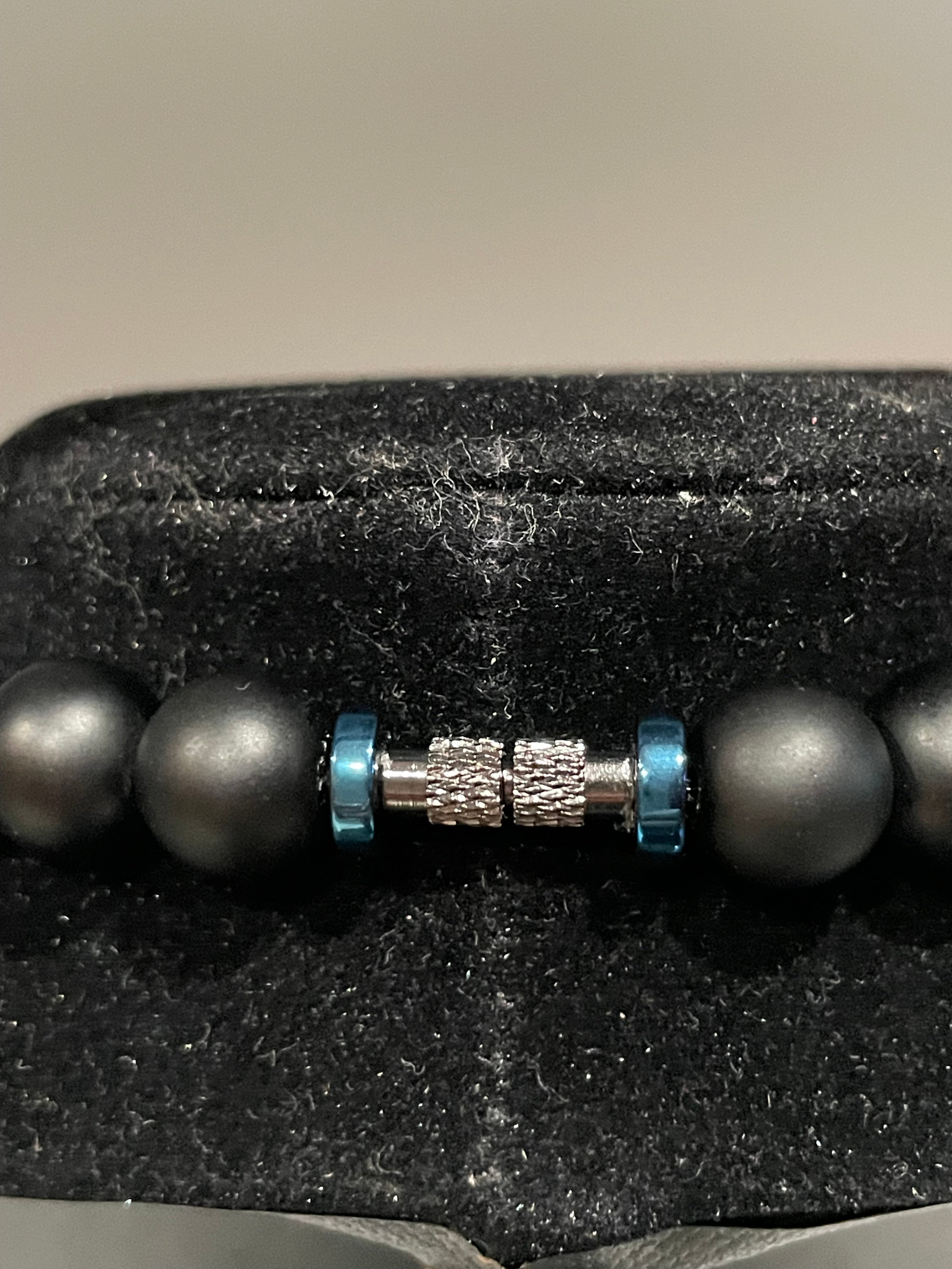 Close-up of a black beaded black metallic screw clasp closure and blue accent on a textured surface.