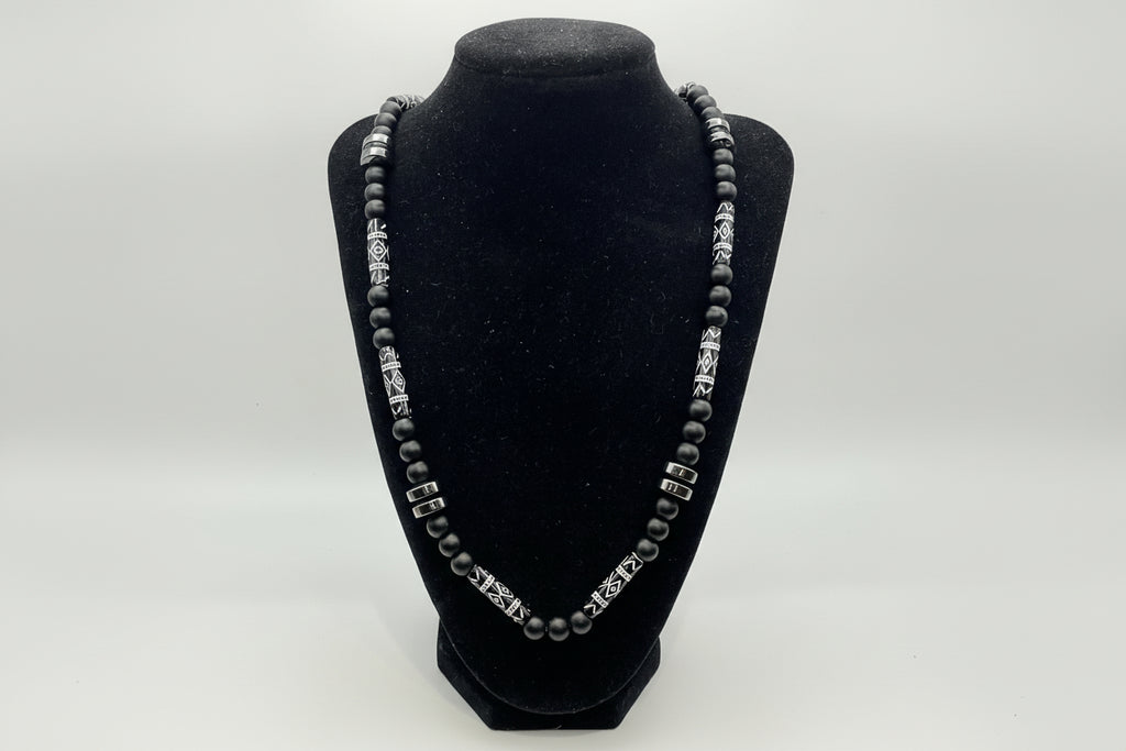 Black beaded bracelet with silver clasp on a black velvet stand against a white background
