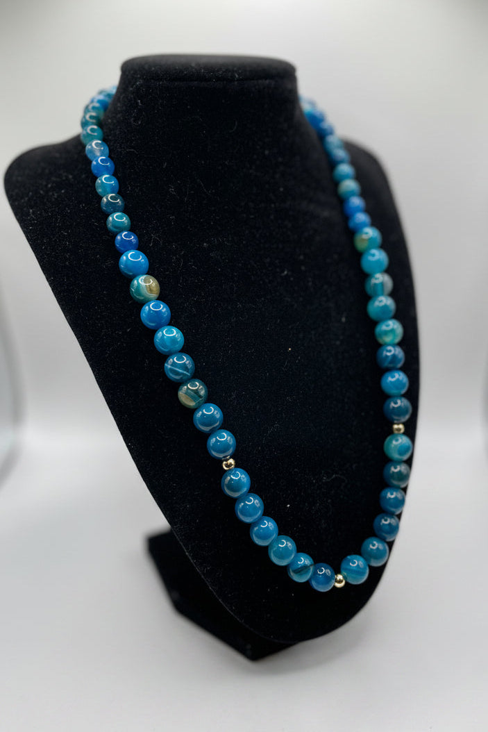 Blue beaded necklace on a black stand with a white background
