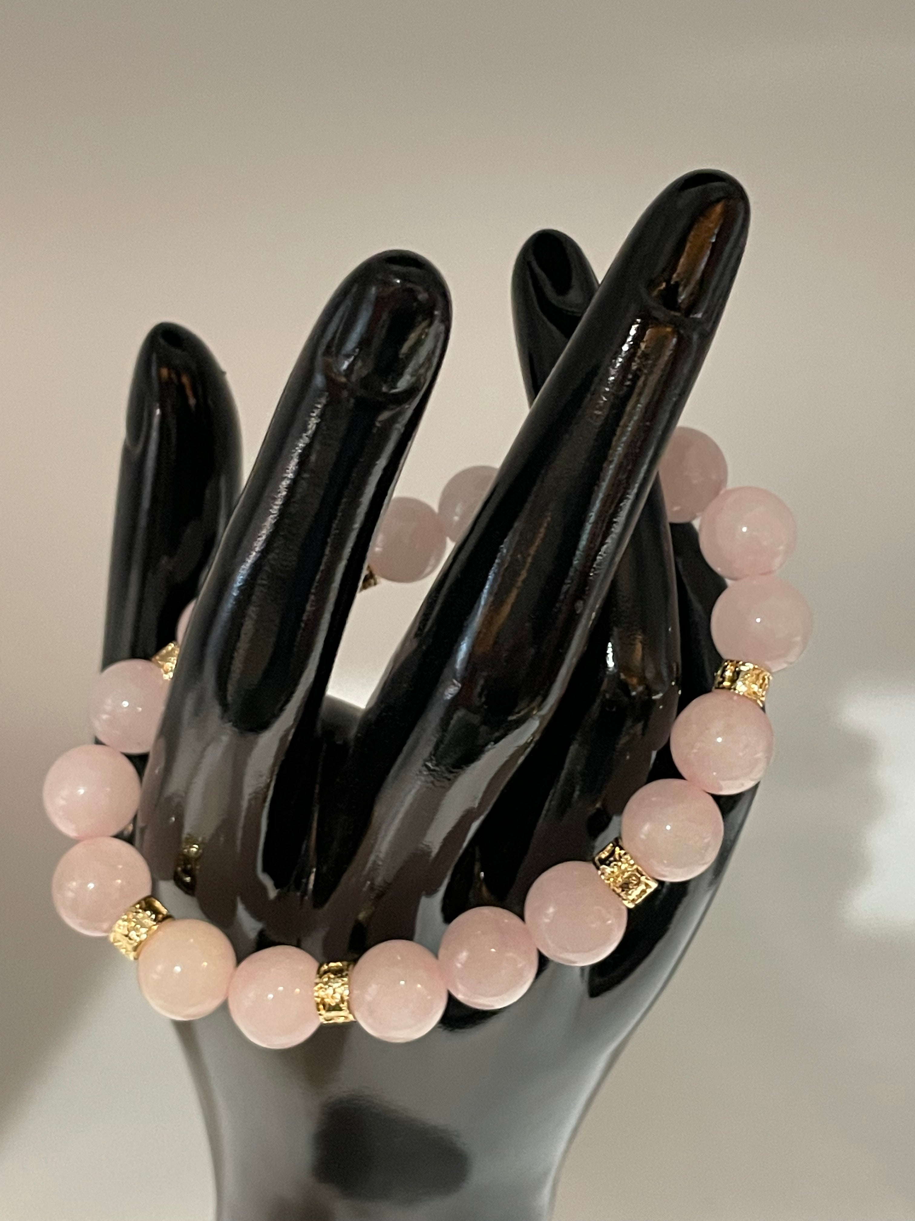 Pink beaded bracelet with gold accents on a black mannequin hand against a neutral background