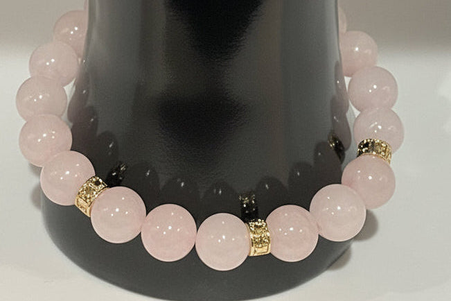 Pink beaded bracelet with gold accents on a reflective surface