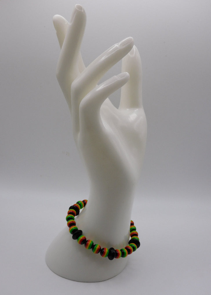 A beaded stretch bracelet with green, yellow, orange, and black beads, displayed on a white ceramic mannequin hand against a light gray background.