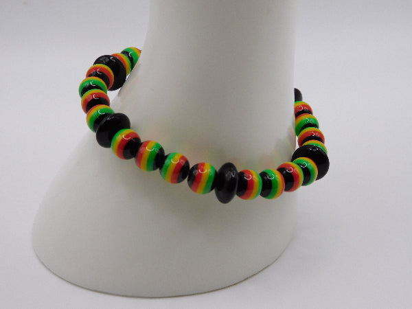 A beaded bracelet with alternating black beads and striped beads in red, yellow, and green, displayed on a white mannequin stand against a light gray background.