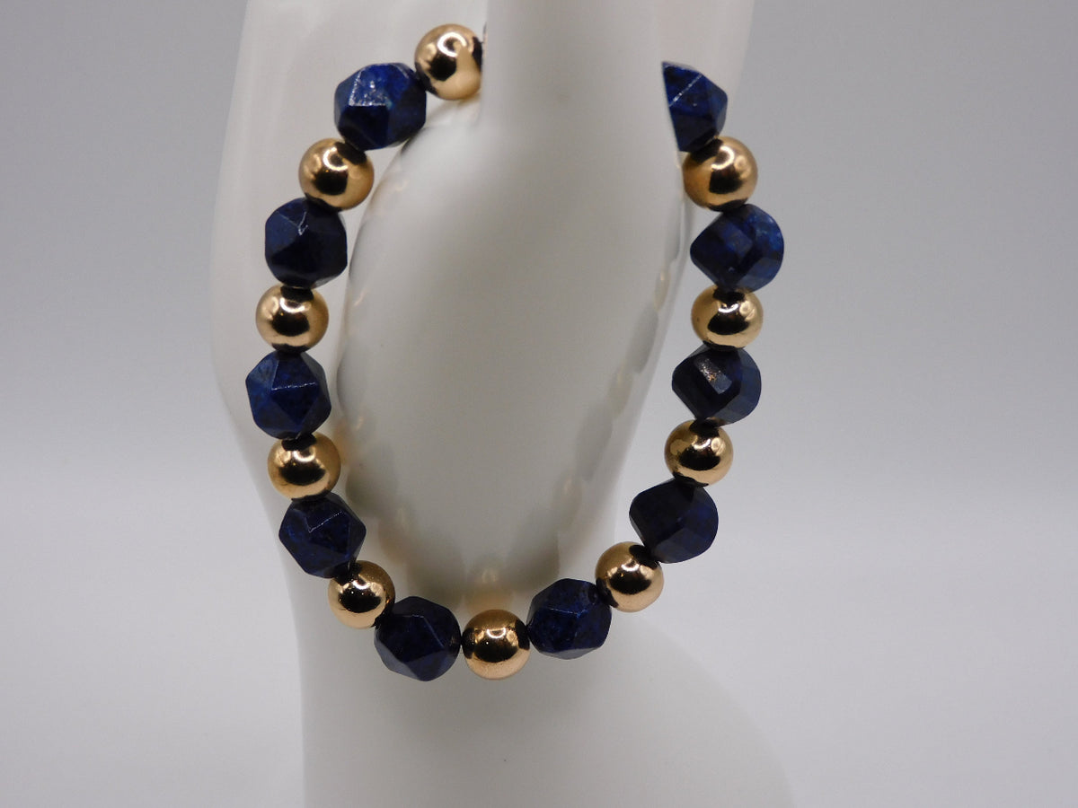 A beaded stretch bracelet displayed on a white mannequin bust. The bracelet features faceted dark blue beads alternating with polished metallic gold beads.