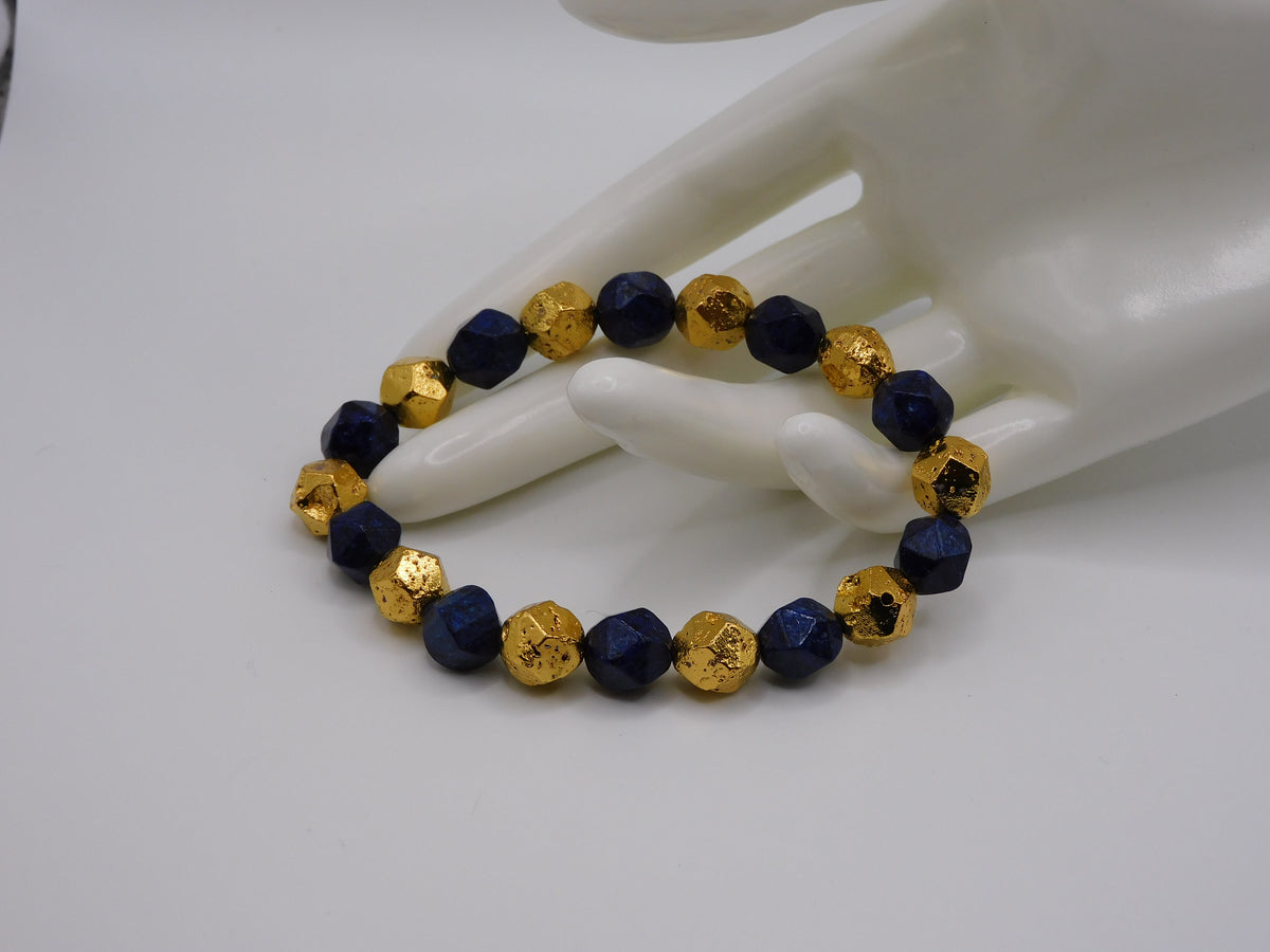 A beaded bracelet with alternating deep navy blue and textured metallic gold faceted beads, displayed on a white ceramic mannequin hand against a plain white background.