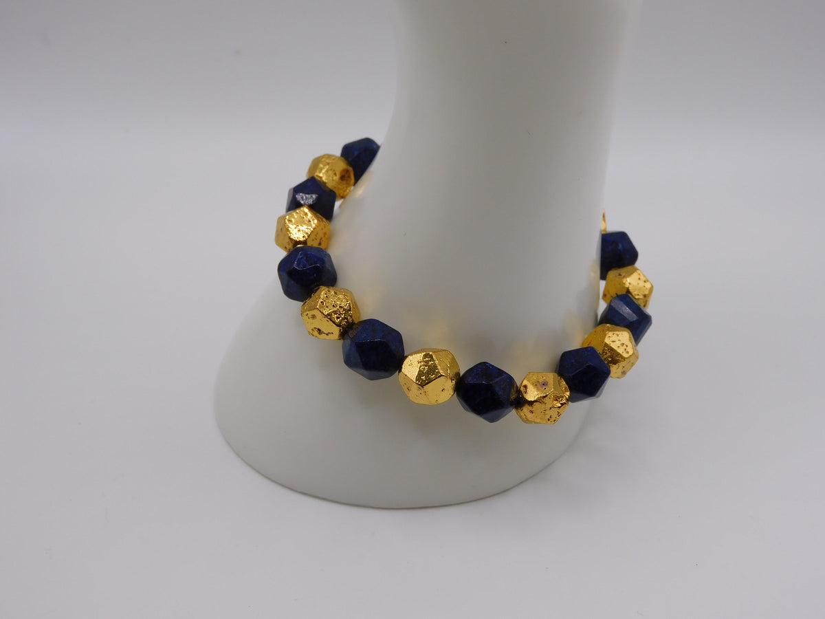 A beaded stretch bracelet with faceted dark blue and textured gold beads, displayed on a white mannequin stand against a light gray background.