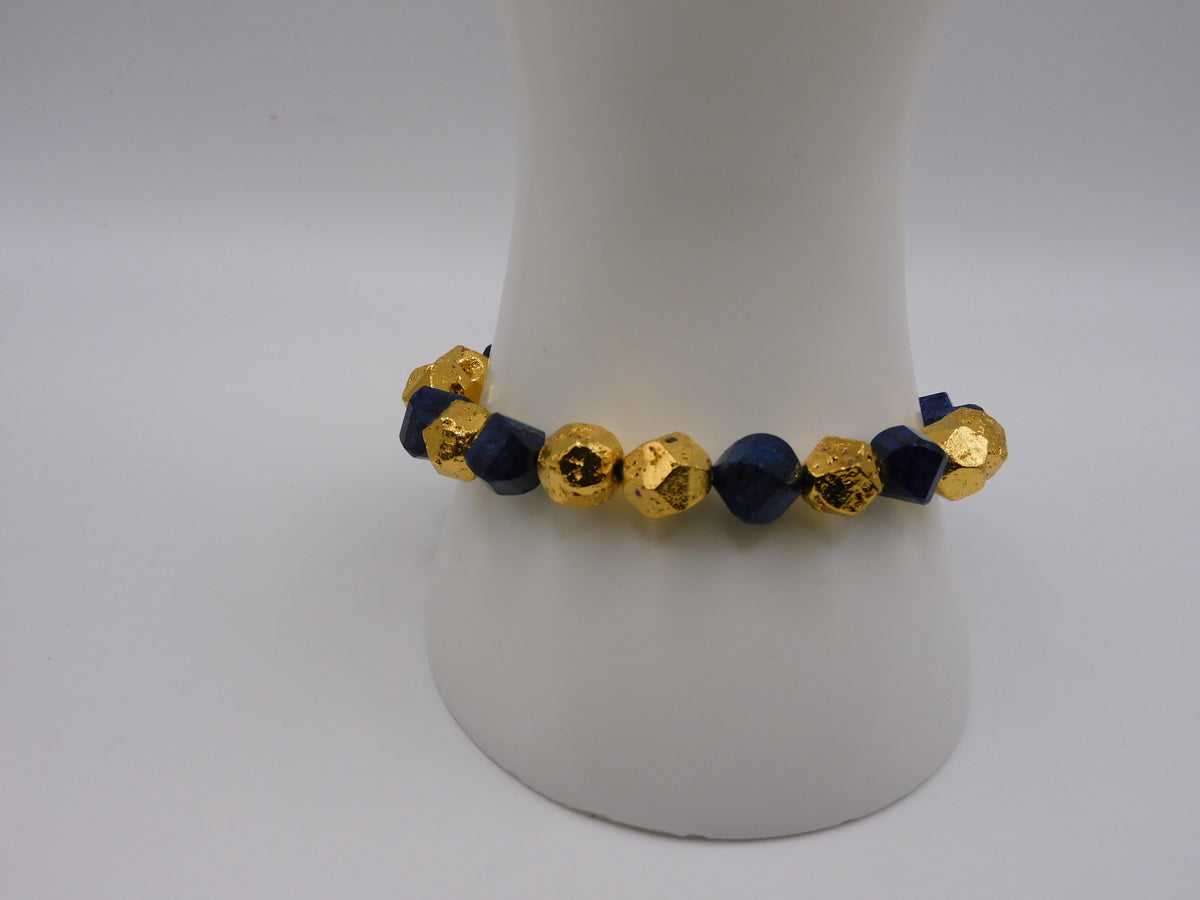 A beaded stretch bracelet featuring alternating faceted gold and dark navy blue beads, displayed on a white mannequin stand against a light gray background.