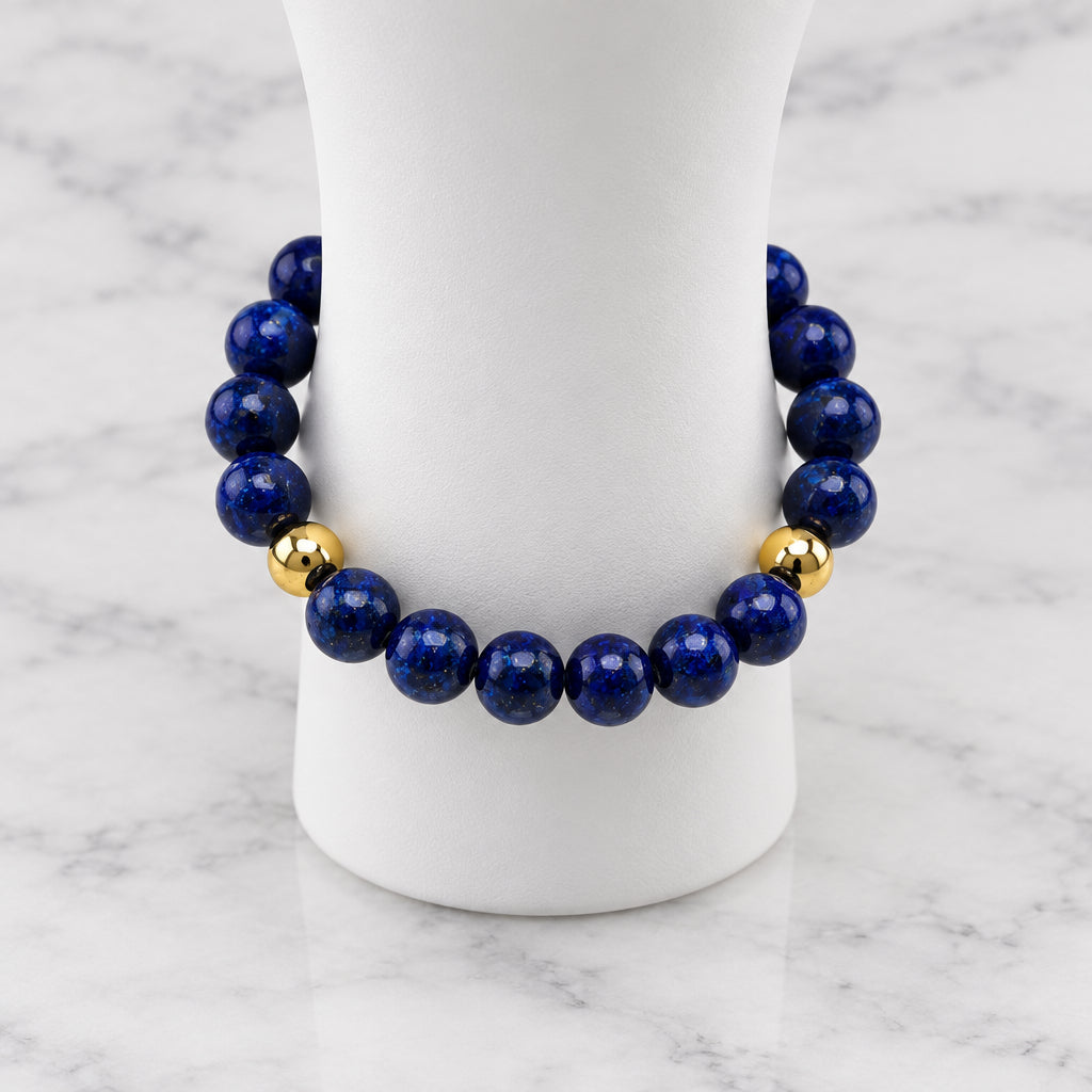 A beaded bracelet made of dark blue lapis lazuli stones with two small gold spacer beads, displayed on a white mannequin stand against a light gray background.