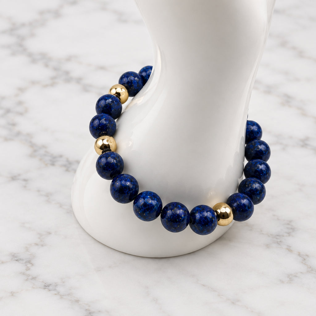 A beaded bracelet with dark blue lapis lazuli-style round beads and small metallic gold spacer beads, displayed on a white mannequin stand against a light gray background.