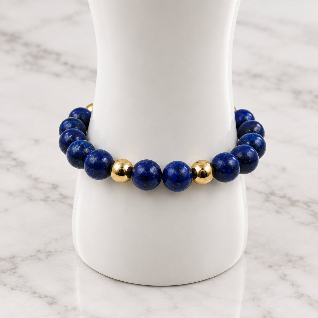 A beaded bracelet made of dark blue lapis lazuli stones with alternating polished gold spacer beads, displayed on a white mannequin stand against a light gray background.