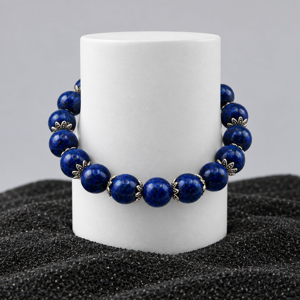 A beaded stretch bracelet made of dark blue lapis lazuli stones separated by small silver-toned metal spacers, displayed on a white cylindrical stand against a light gray background.