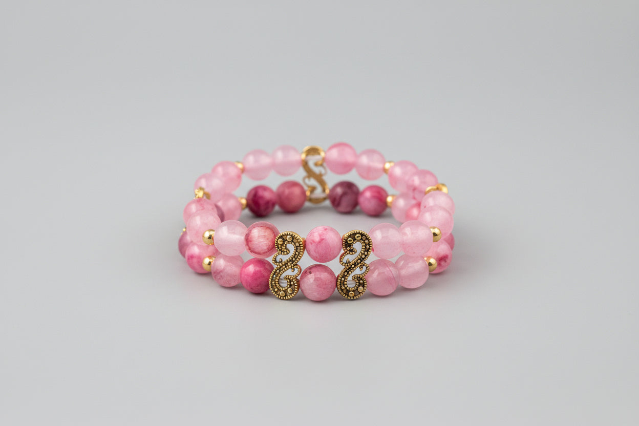 Pink beaded bracelet with gold charms on a wooden surface