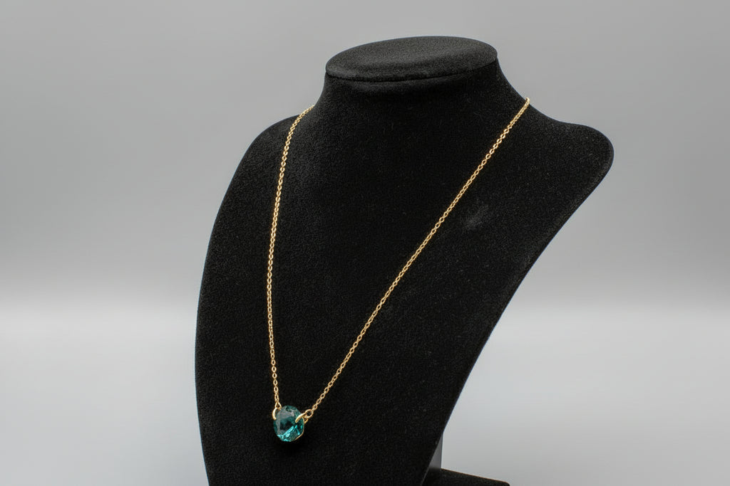 Black stand with a gold chain and green gemstone on a reflective surface