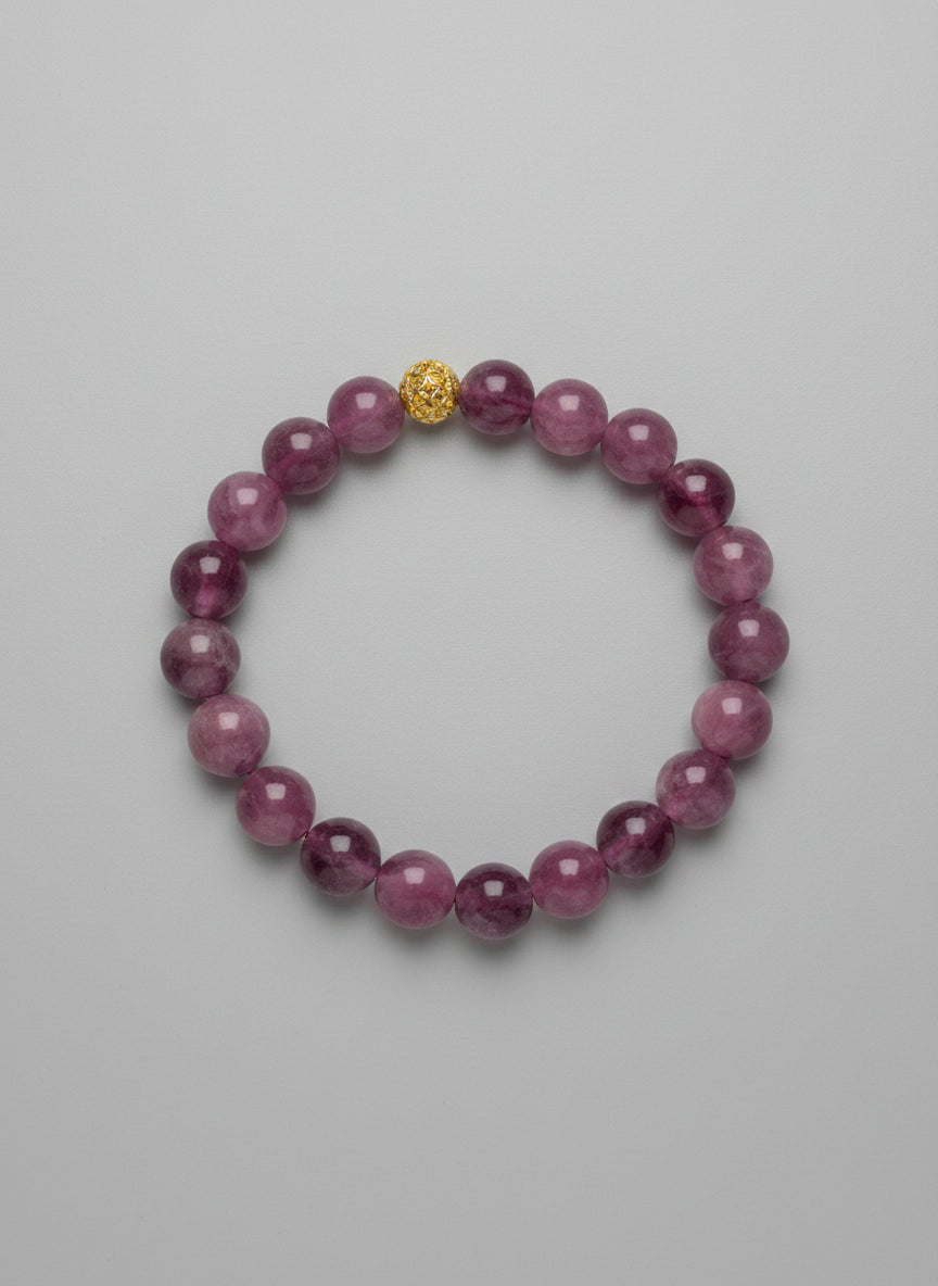 Purple beaded bracelet with a gold charm on a wooden surface