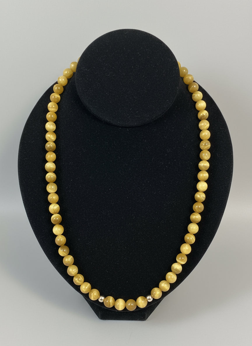Yellow beaded necklace on a black stand with goldtone charm 