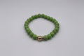 Green beaded bracelet with a gold accent on a light gray background