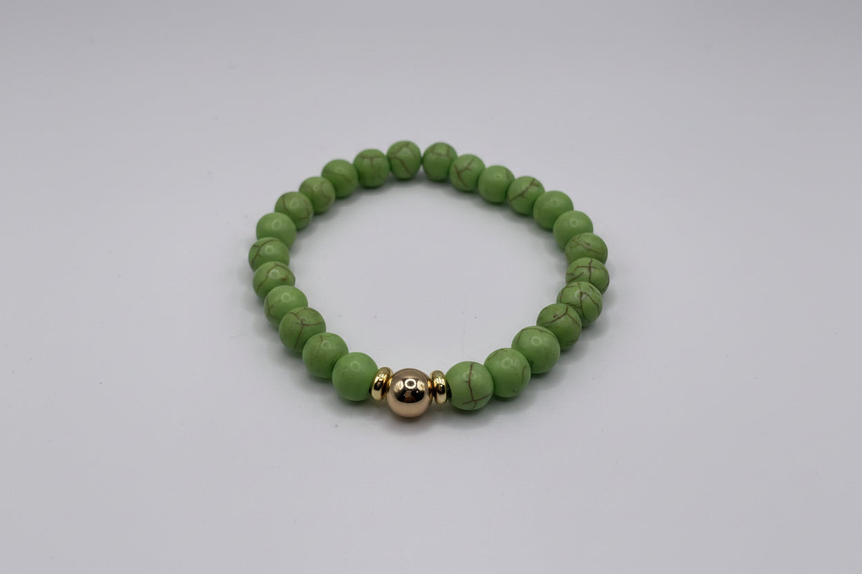 Green beaded bracelet with a gold accent on a light gray background