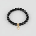 Black beaded bracelet with a heart-shaped charm on a wooden surface