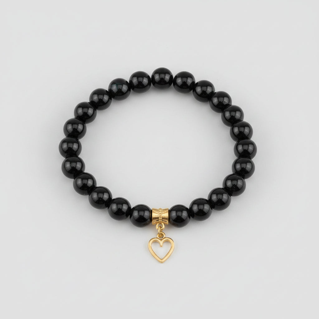 Black beaded bracelet with a heart-shaped charm on a wooden surface