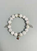White beaded bracelet with silver charms on a textured surface