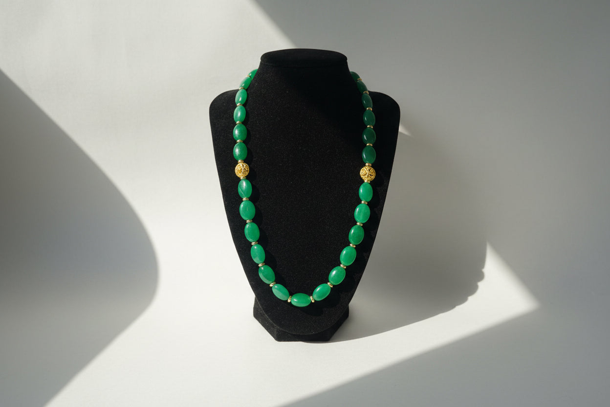 Green beaded necklace with gold accents on a black stand against a white background