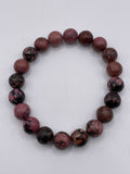 Round beaded bracelet with purple and black stones on a white background