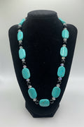 Turquoise beaded necklace on a black velvet stand against a white background