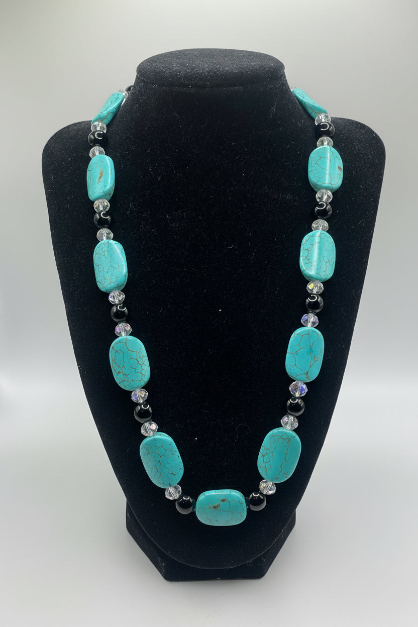 Turquoise beaded necklace on a black velvet stand against a white background