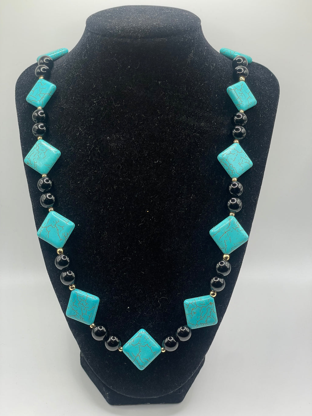 Necklace with turquoise square beads on a black display stand
