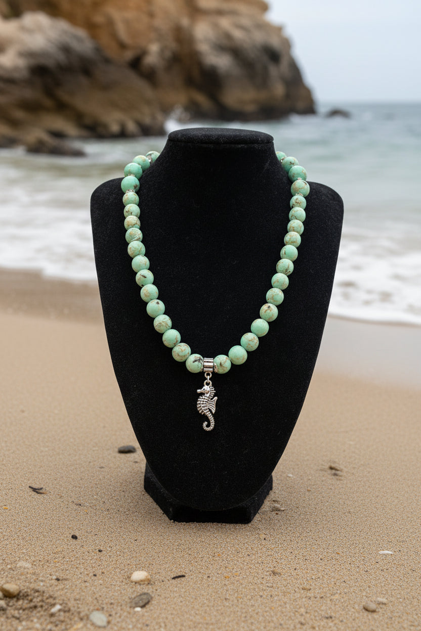Necklace with turquoise beads and a silver seahorse charm on a black bust against a white background