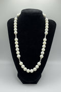 A white pearl necklace with silver-toned chain links, displayed on a black velvet jewelry bust against a light gray background.
