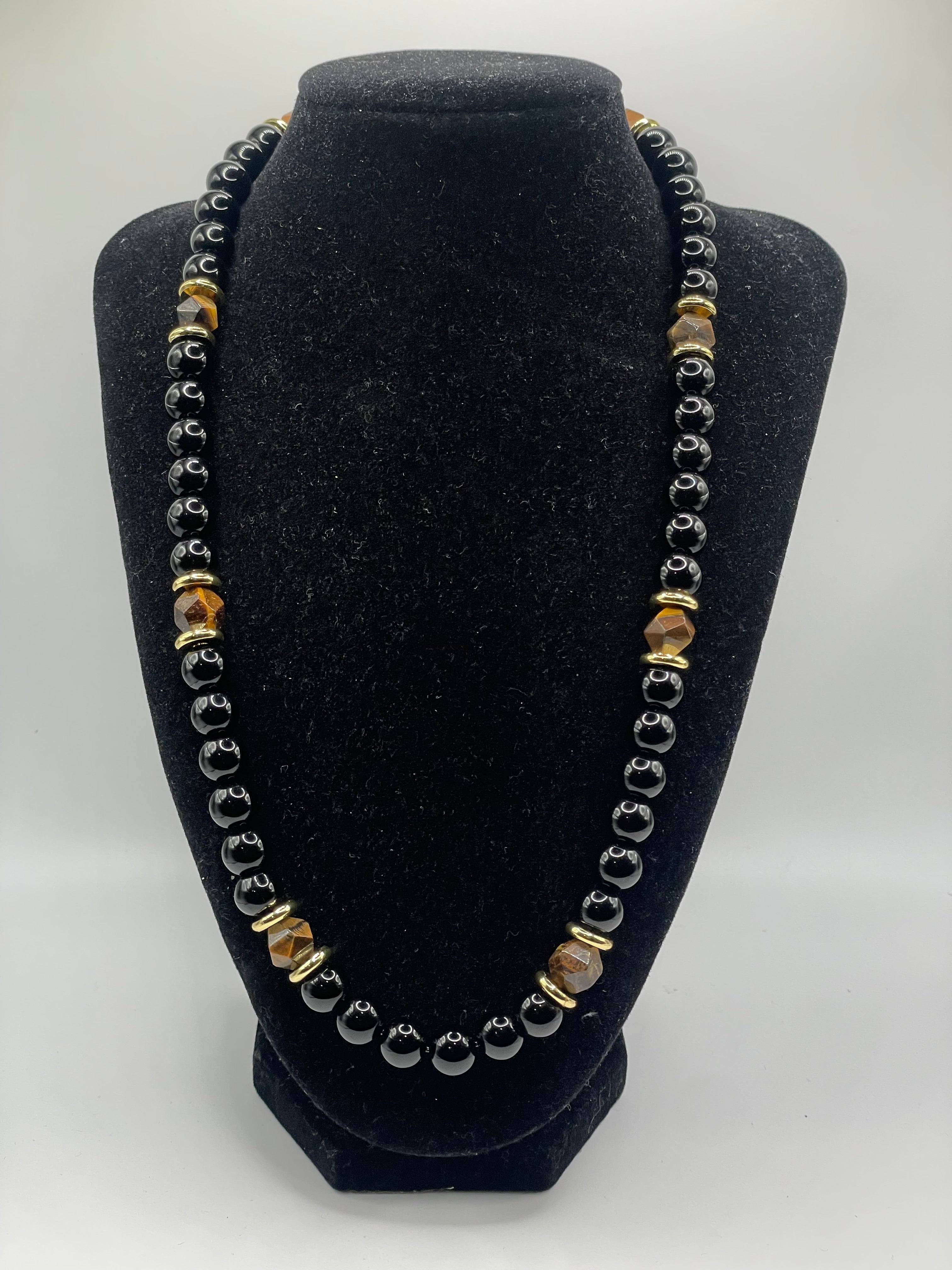 Bracelet with gold and silver beads on a black stand against a white background
