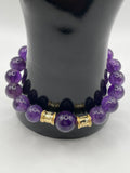 Purple beaded bracelet with gold accents on a black mannequin hand against a white background
