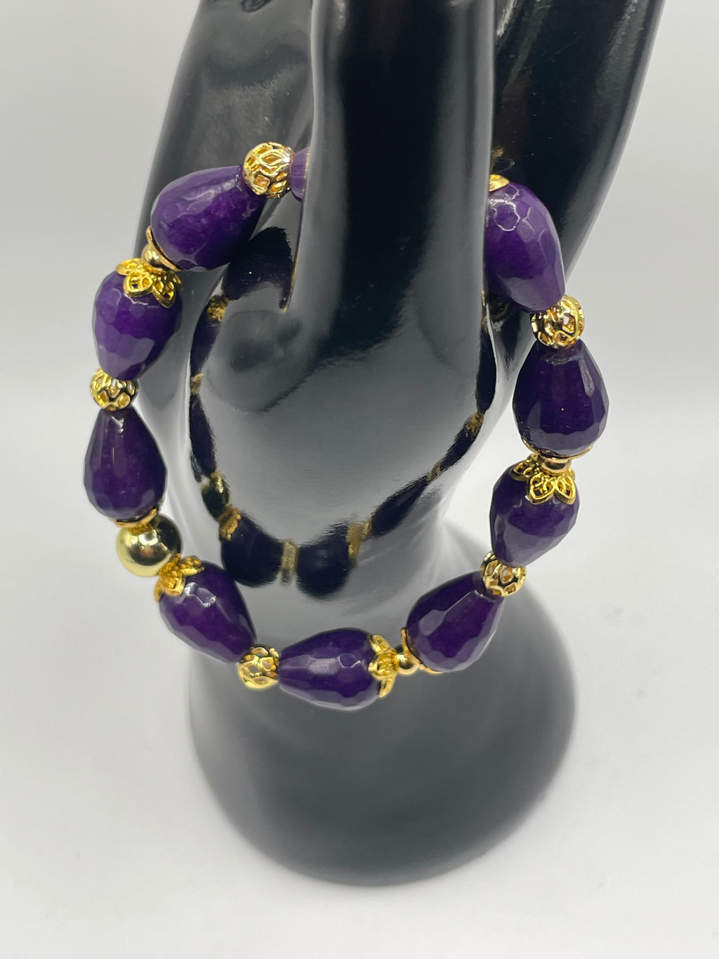 Purple beaded bracelet with gold accents on a black mannequin hand.