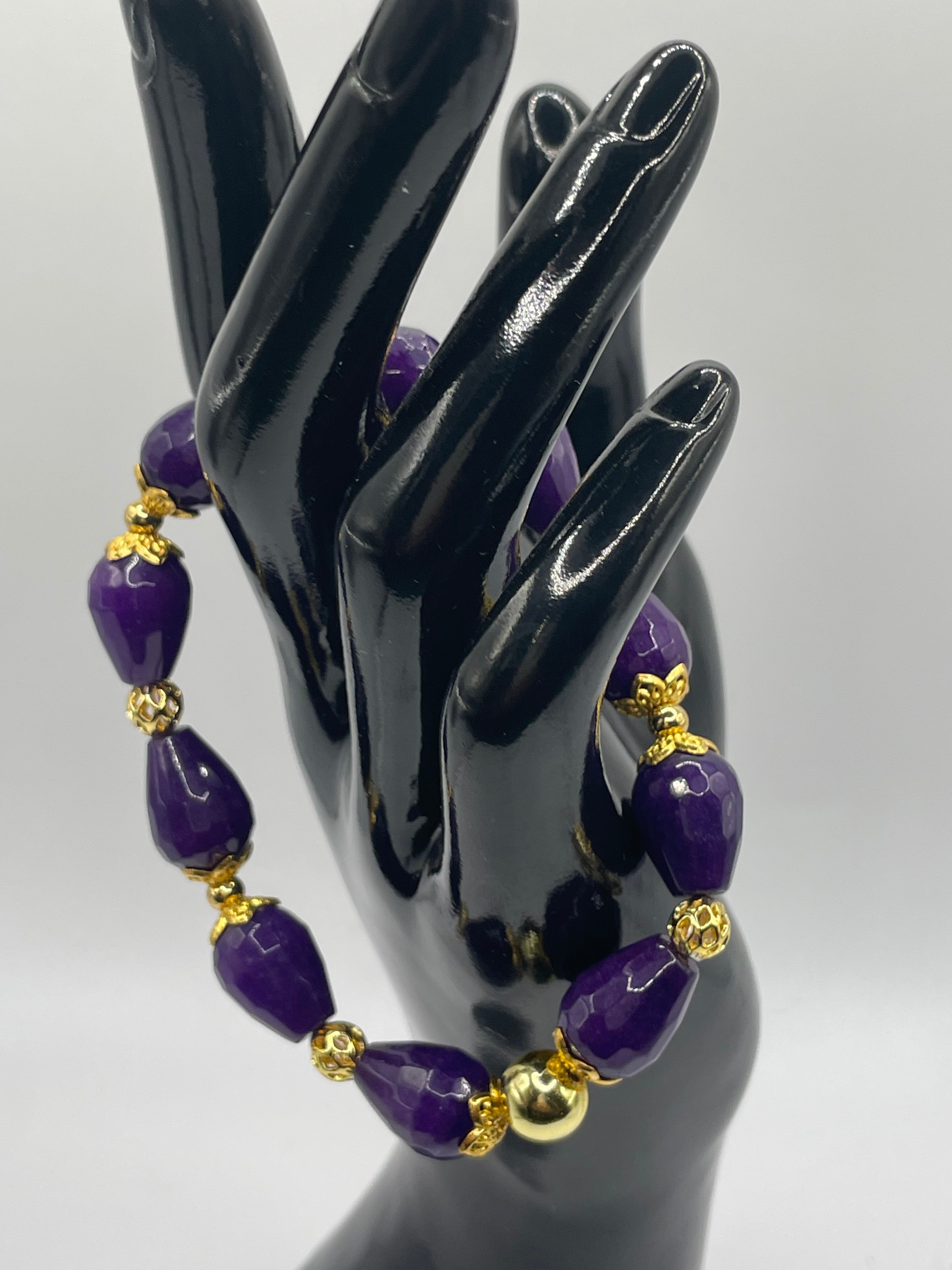 Purple beaded bracelet with gold accents on a black mannequin hand against a white background