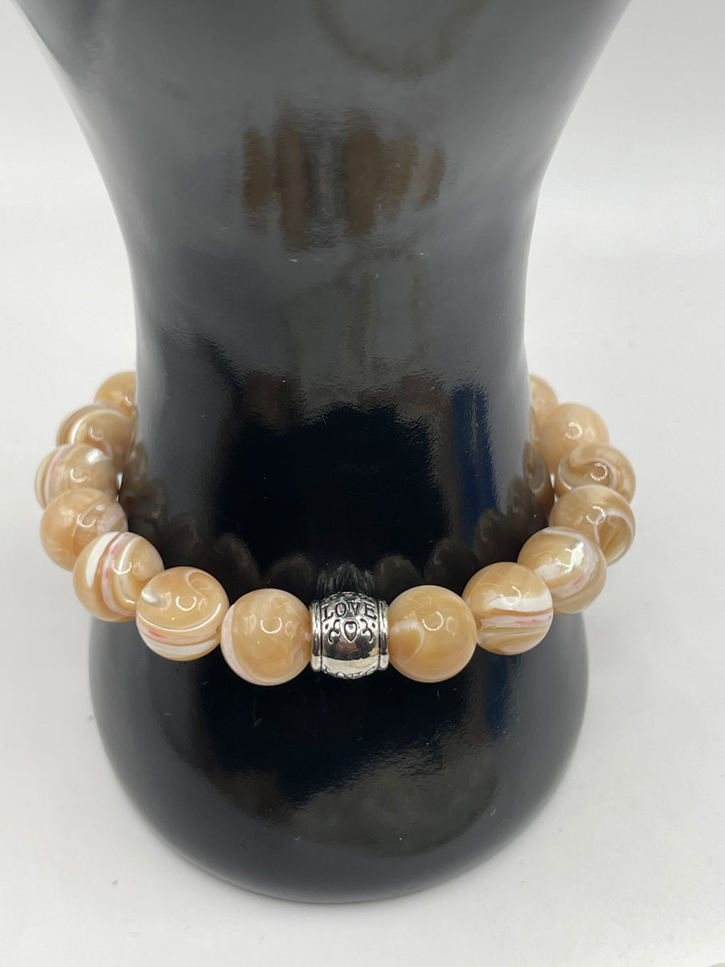 Beige beaded bracelet with a silver charm on a dark surface