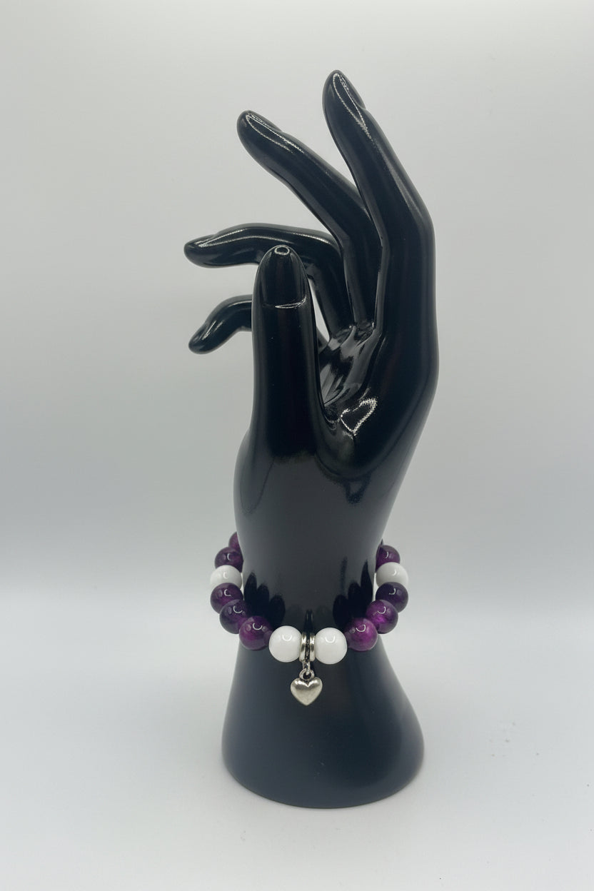 Black hand holding a bracelet with purple and white beads on a white background