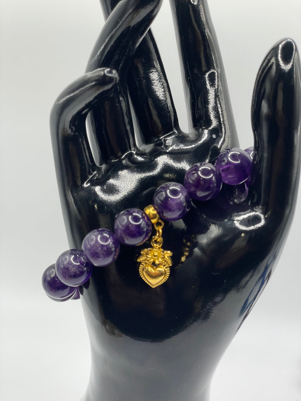 Purple beaded bracelet with a gold charm on a black mannequin hand against a white background
