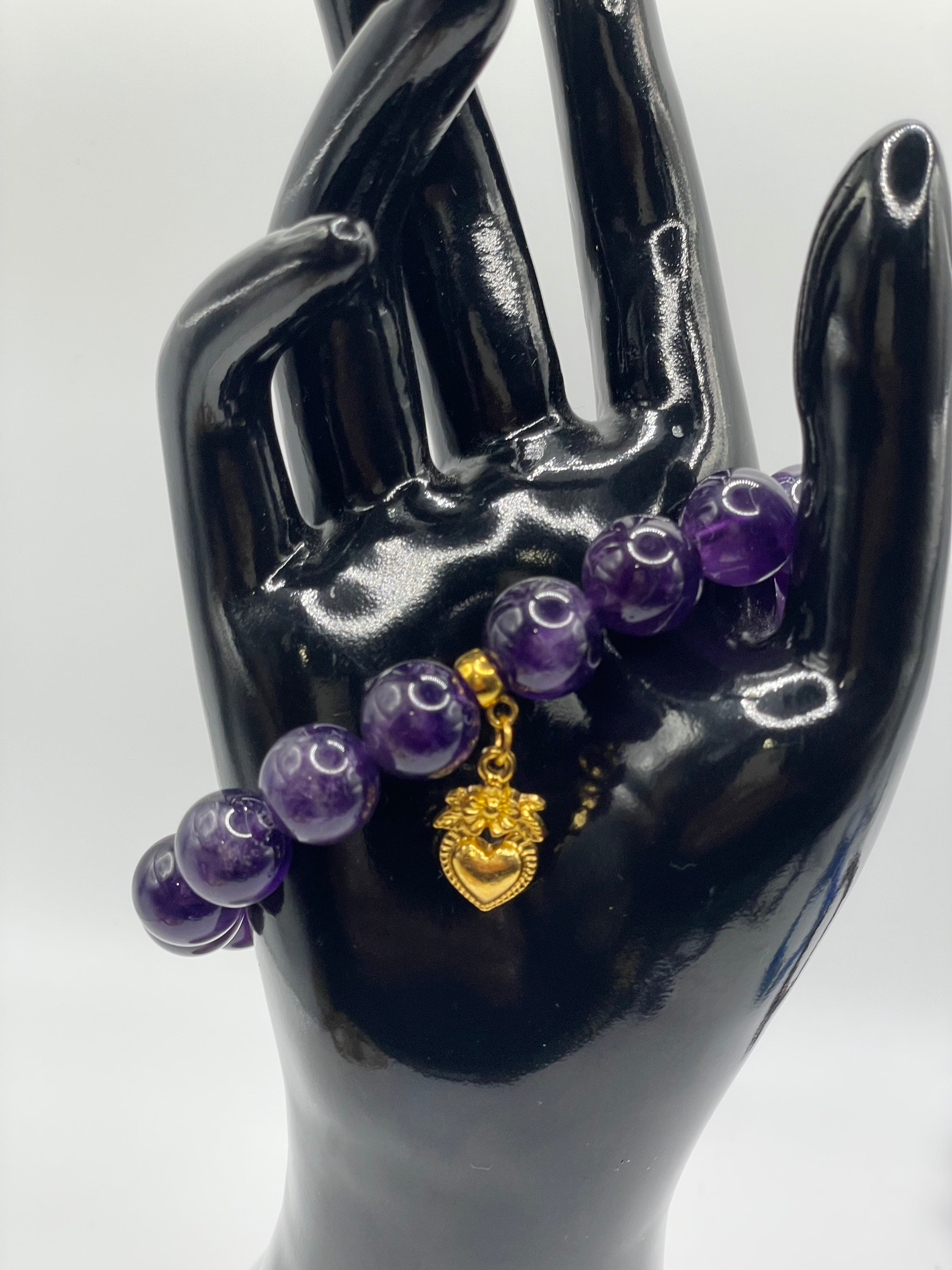 Purple beaded bracelet with a gold charm on a black mannequin hand against a white background