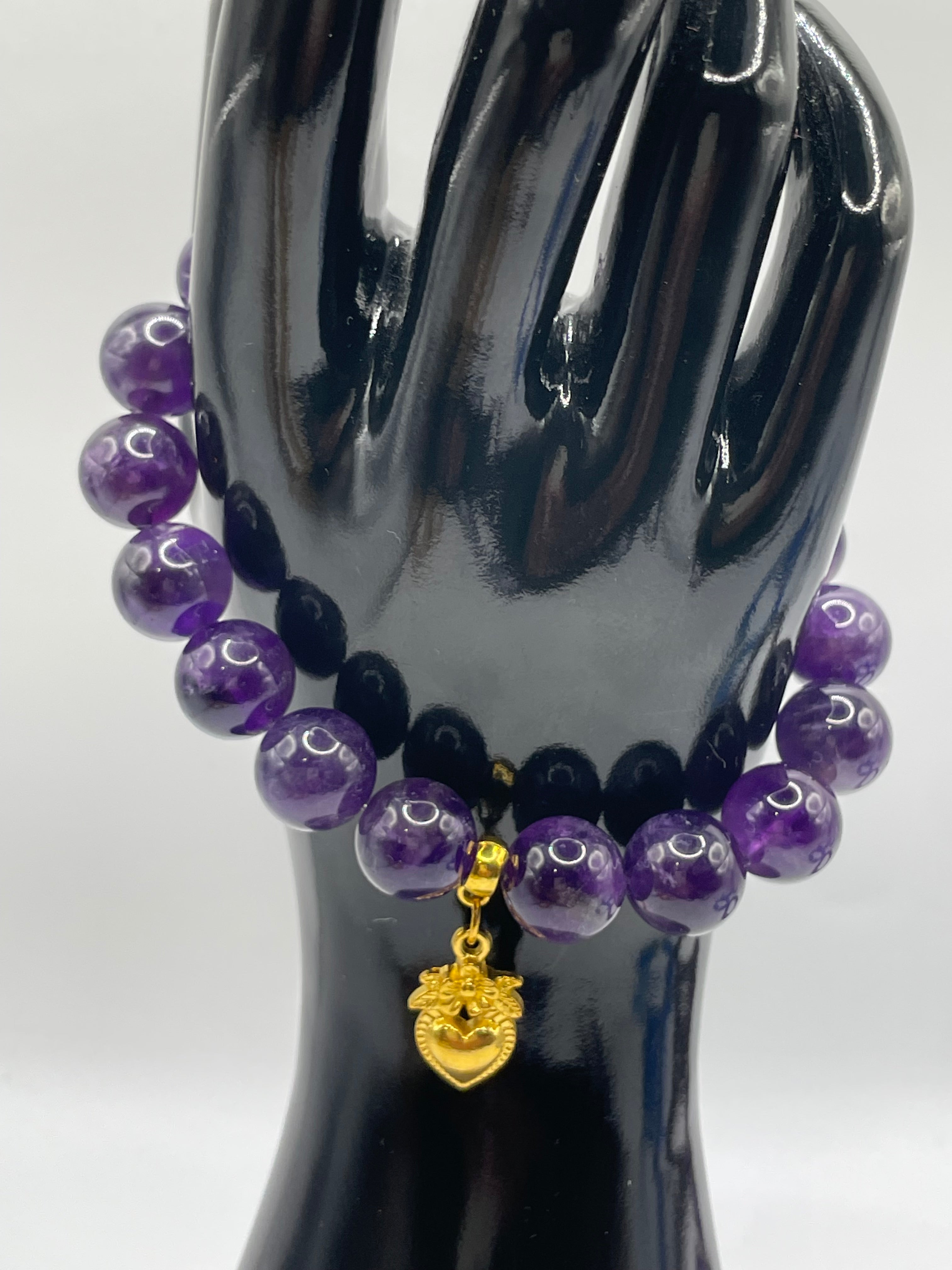 Purple beaded bracelet with a gold charm on a black mannequin hand against a white background