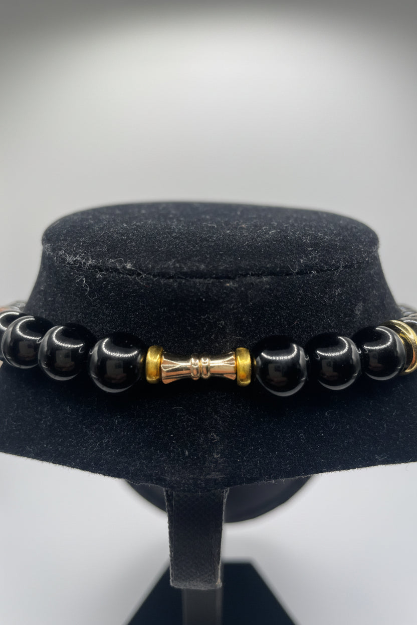 Black beaded necklace view with gold accents on a black stand against a white background