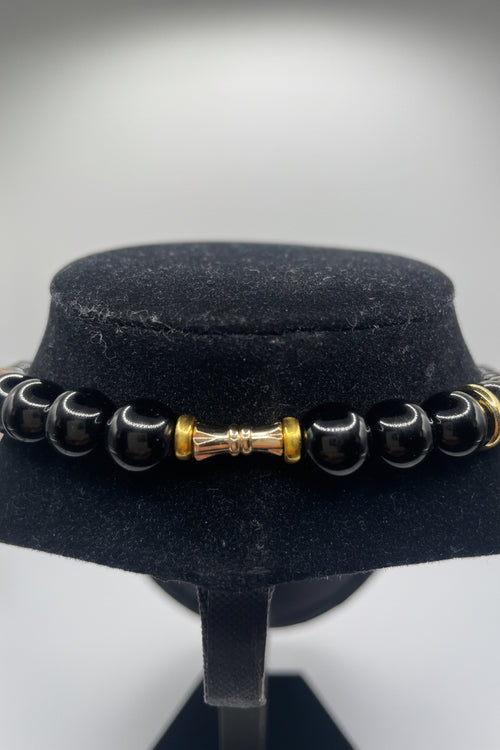 Black beaded necklace view with gold accents on a black stand against a white background