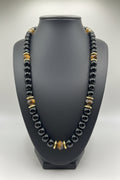 Necklace with black, gold, and clear beads on a gray bust