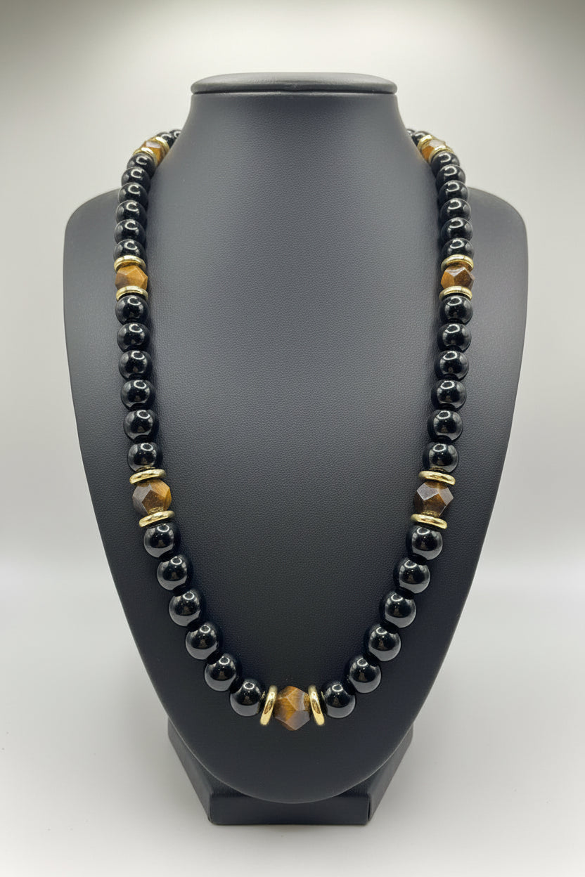 Necklace with black, gold, and clear beads on a gray bust