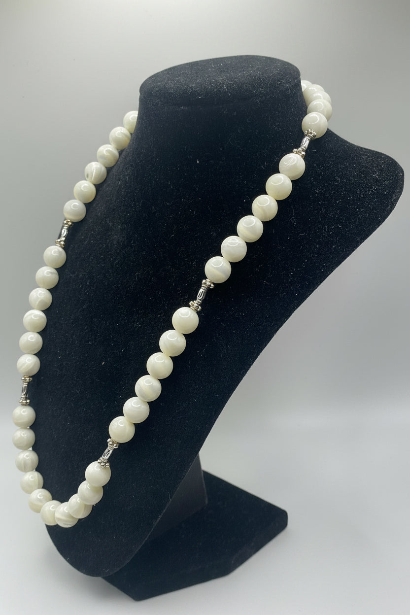 A strand of white pearl-like round beads with small silver spacer details, draped over a black velvet jewelry display bust on a light gray background.